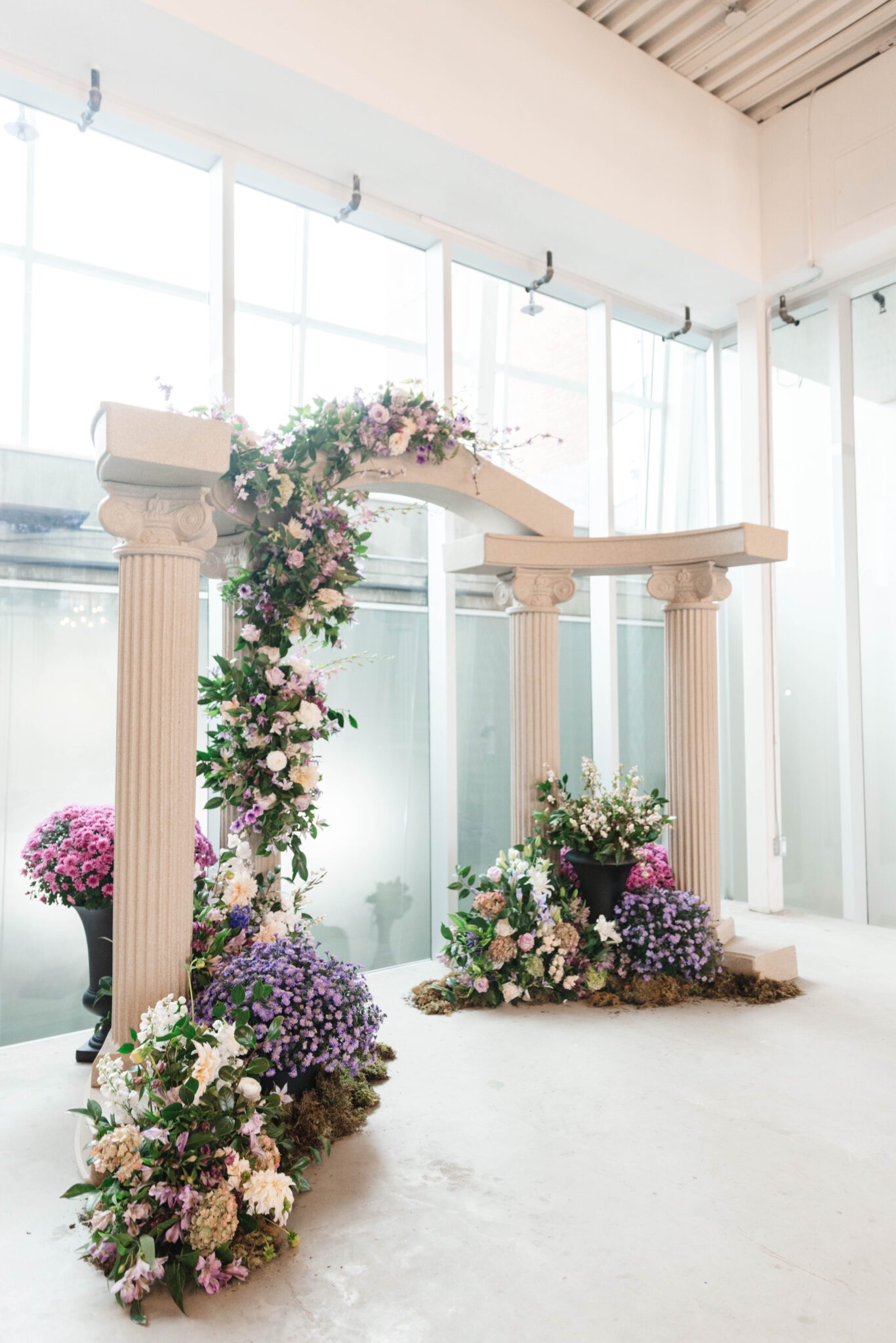 Purple garden wedding ceremony at historic venue The Pendennis in Edmonton, Alberta. Lush purple garden-inspired florals. Architectural column archway, with cascading floral installation. 