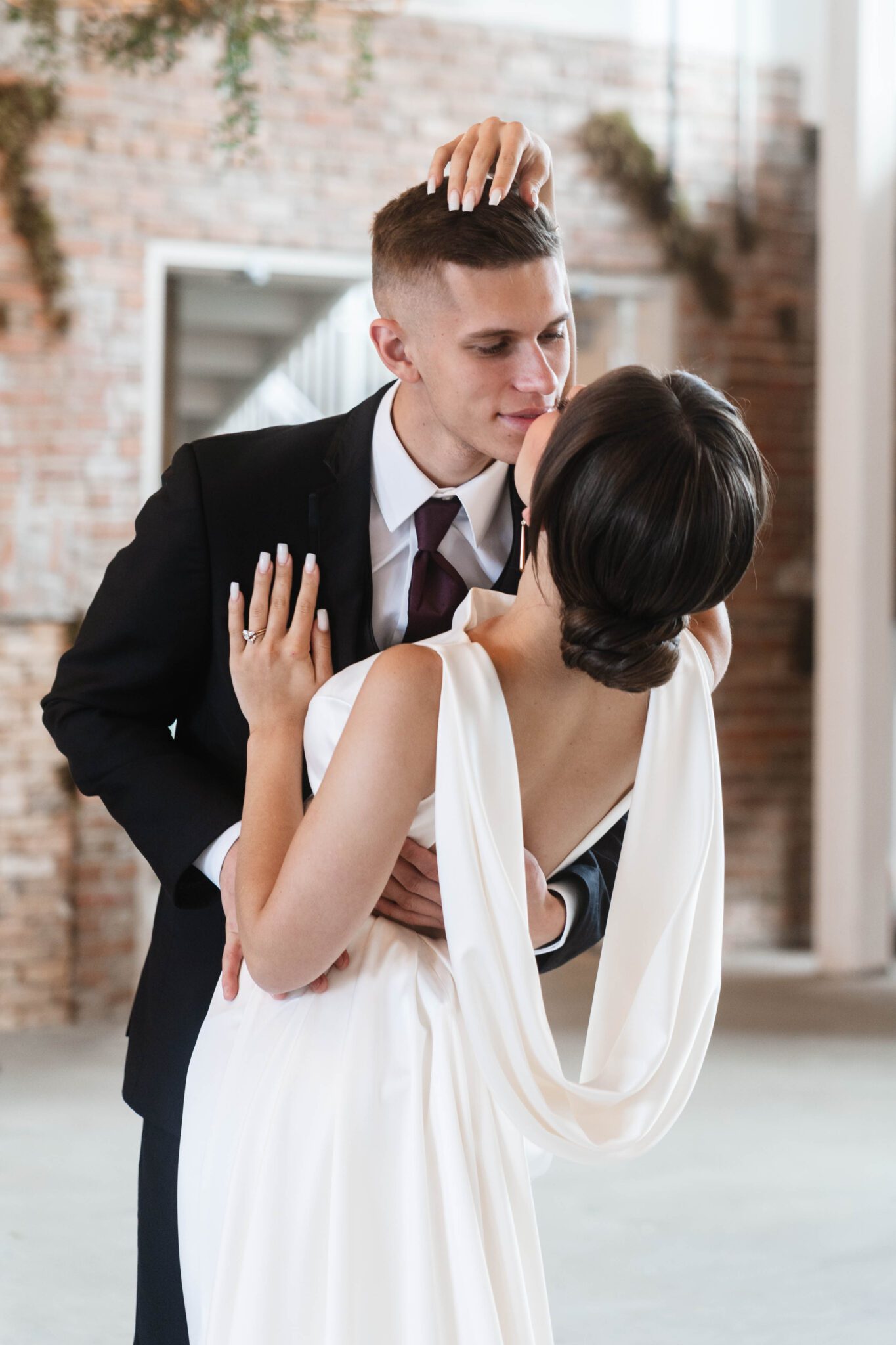 Sophisticated couple embracing during garden-inspired wedding at historic venue The Pendennis in Edmonton, Alberta. Bride wearing a sleek bridal gown with draping fabric in the back. 