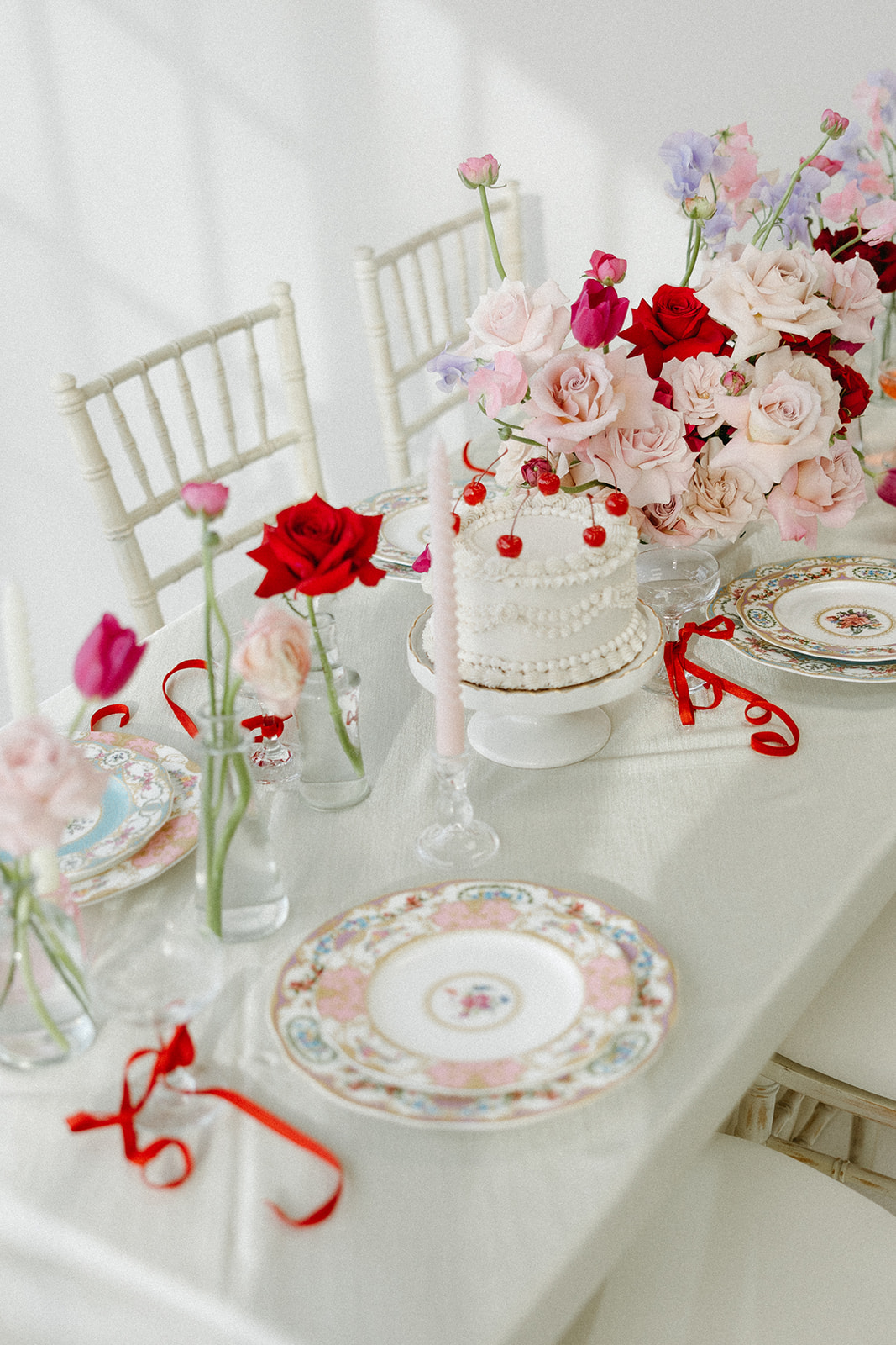 Funky reception setup with vibrant retro-inspired decor and playful design elements like beautiful vintage china, bold coloured candles, and modern flowers. Trendy vintage buttercream wedding cake design with white piped buttercream and cherries on top, perfect for a retro or vintage style wedding.