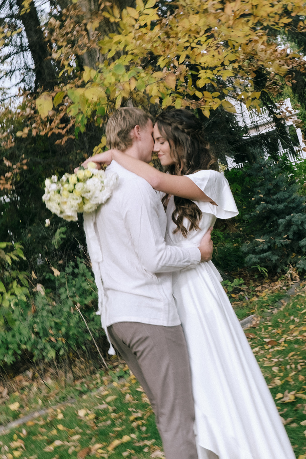 Bride and groom share a romantic moment under a canopy of trees at a casual backyard wedding with a cottage core theme. Bride wearing casual but feminine wedding dress from By Catalfo.
