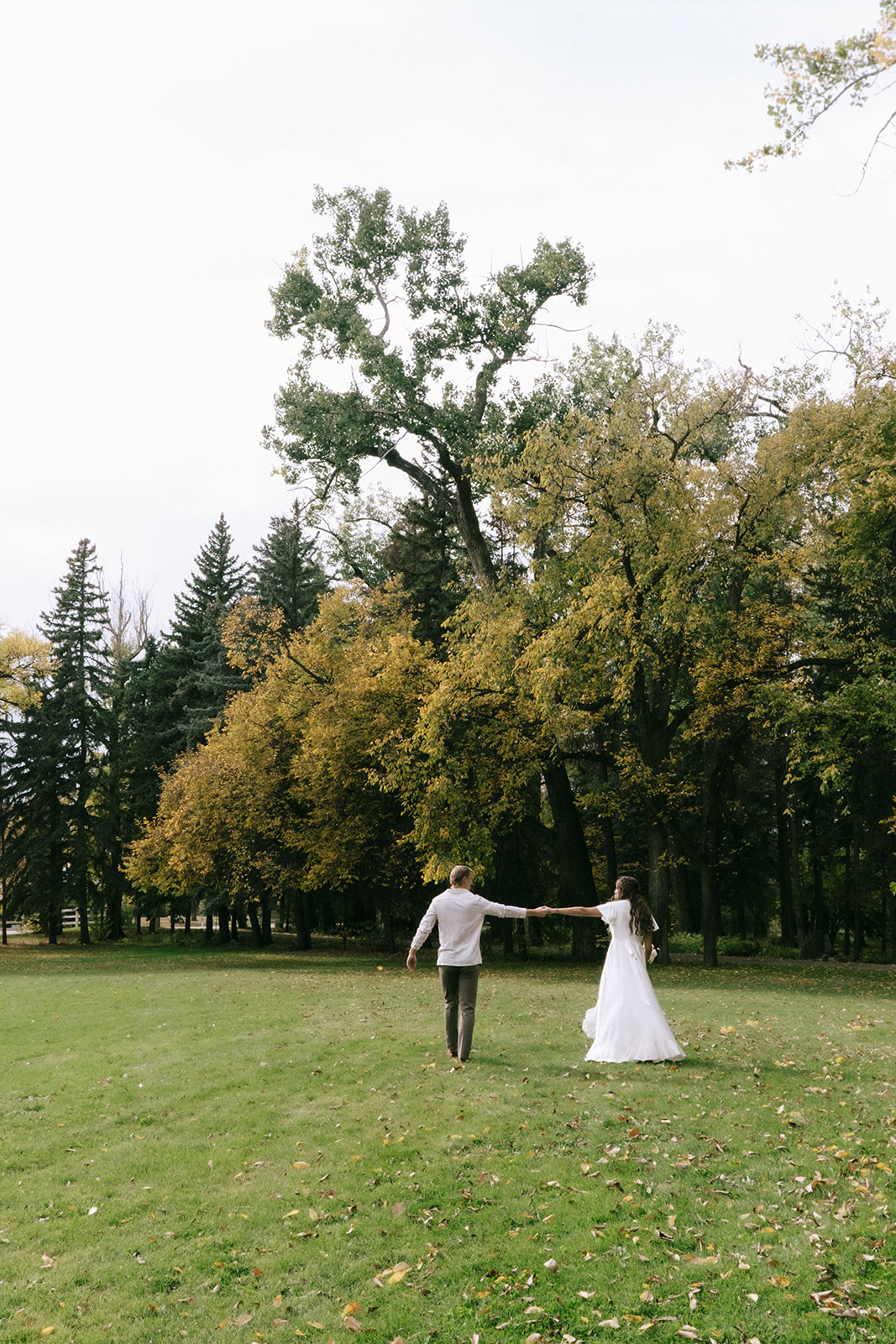 Bride and groom share a romantic moment under a canopy of trees at a casual backyard wedding with a cottage core theme. Bride wearing casual but feminine wedding dress from By Catalfo.
