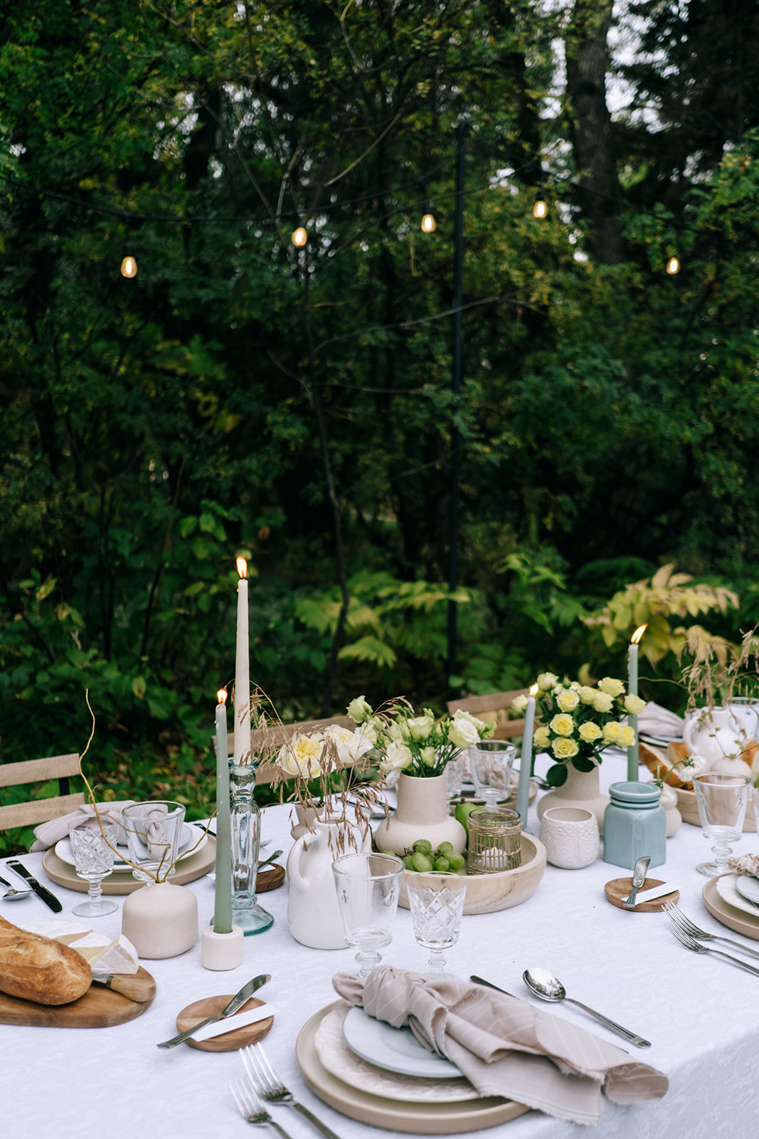 Romantic wedding tablescape featuring earthy grasses, pale yellow florals, wine, and family-style dining under soft candlelight.