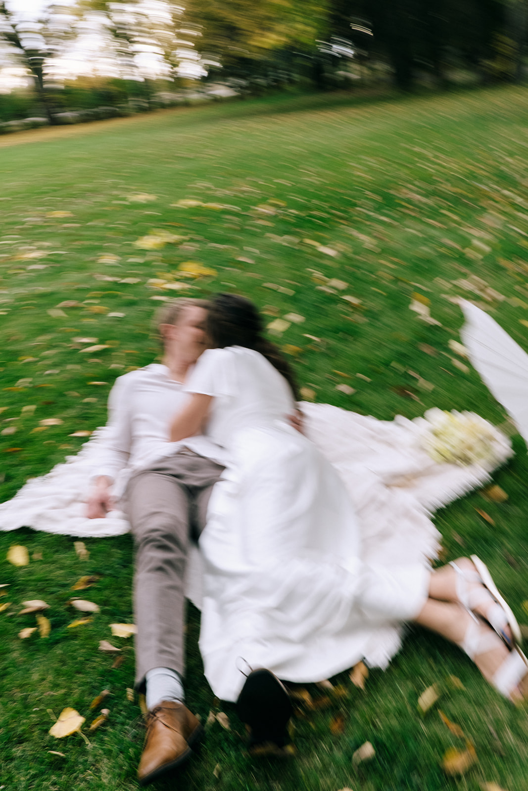 Bride and groom share a romantic moment under a canopy of trees during a summer wedding. Featuring outdoor portraits with white paper parasol and pale yellow bouquet.