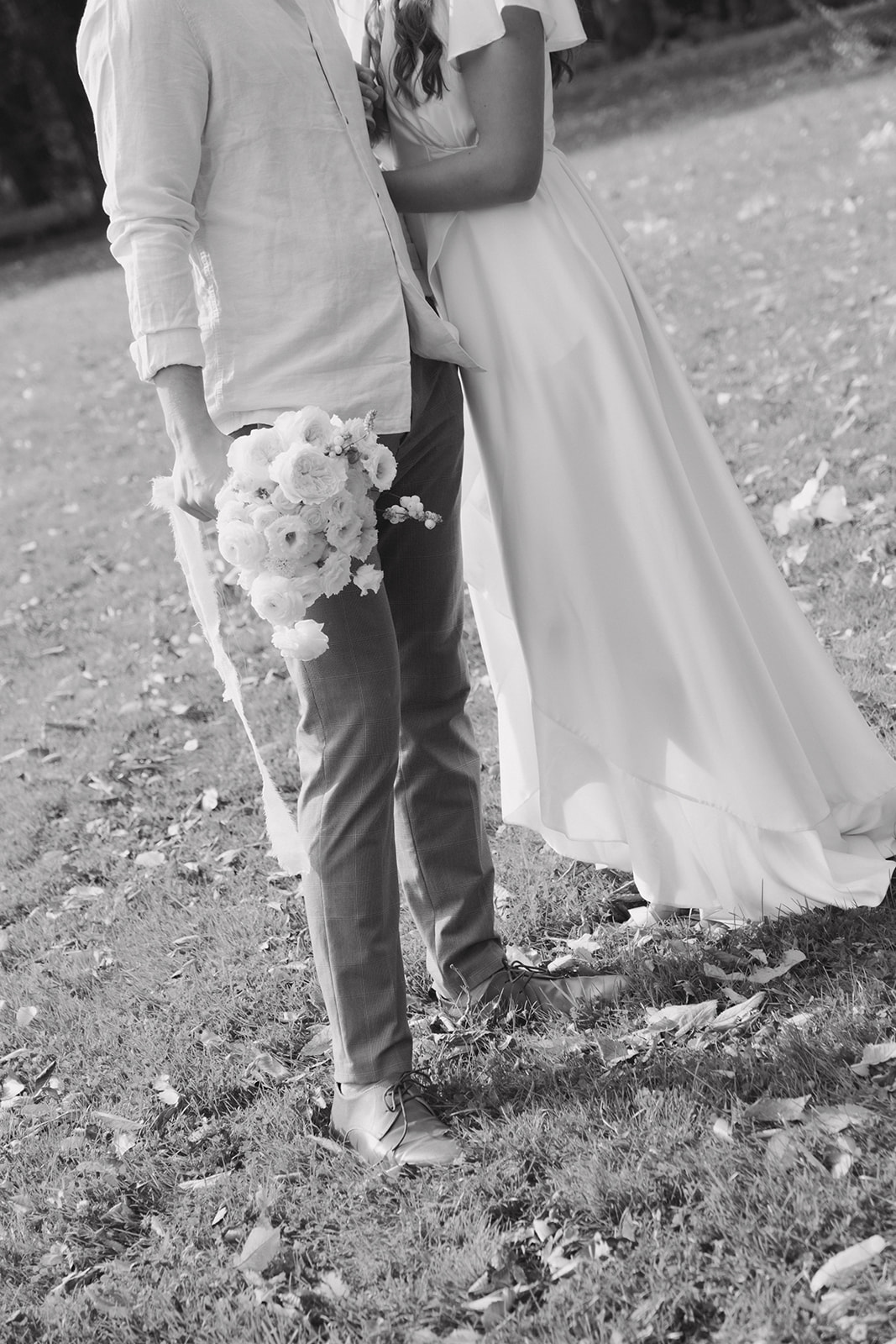 Bride and groom share a romantic moment under a canopy of trees during a summer wedding. Featuring outdoor portraits with white paper parasol and pale yellow bouquet.