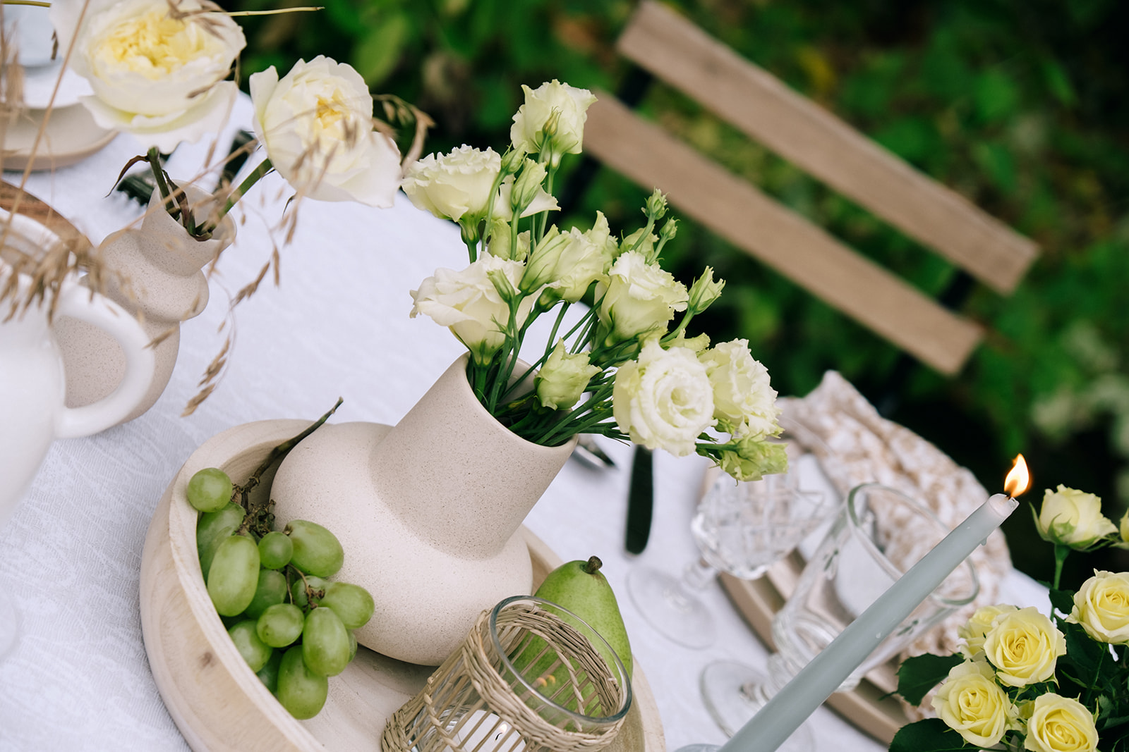 Romantic wedding tablescape featuring earthy grasses, pale yellow florals, wine, and family-style dining under soft candlelight.