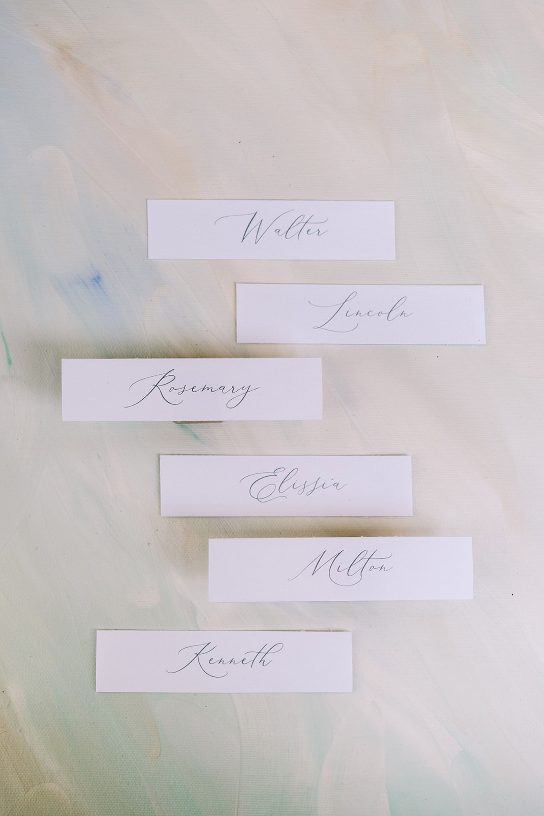 Close-up of wedding place cards with calligraphy on a handpainted misty green flatlay mat. 