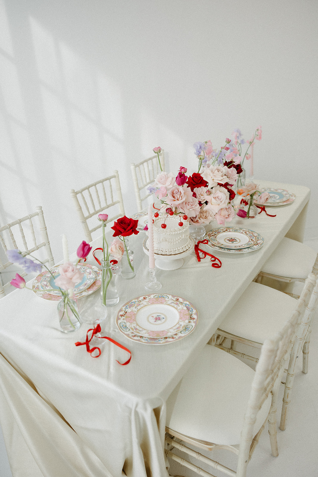 Funky reception setup with vibrant retro-inspired decor and playful design elements like beautiful vintage china, bold coloured candles, and modern flowers. Trendy vintage buttercream wedding cake design with white piped buttercream and cherries on top, perfect for a retro or vintage style wedding.