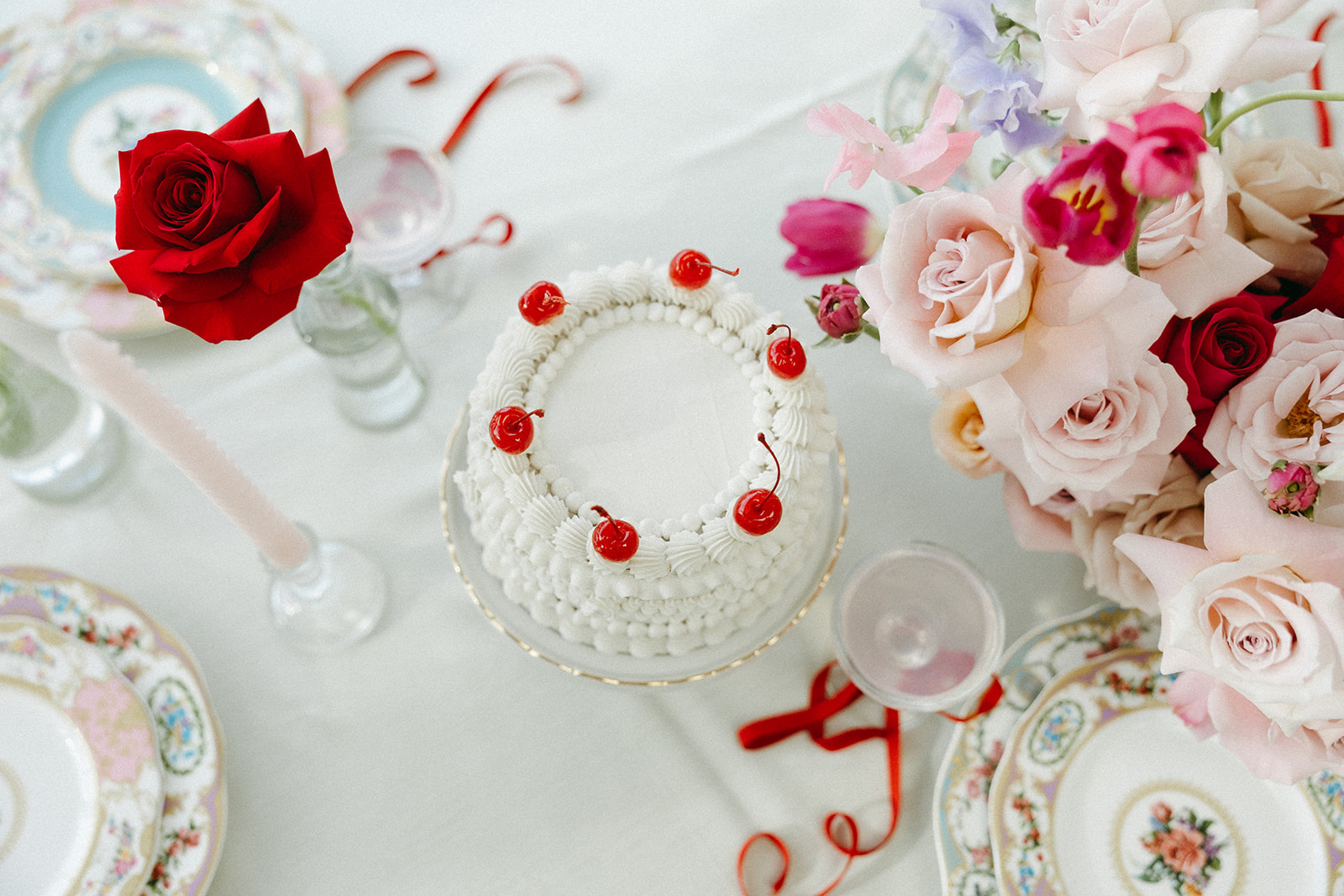 Funky reception setup with vibrant retro-inspired decor and playful design elements like beautiful vintage china, bold coloured candles, and modern flowers. Trendy vintage buttercream wedding cake design with white piped buttercream and cherries on top, perfect for a retro or vintage style wedding.