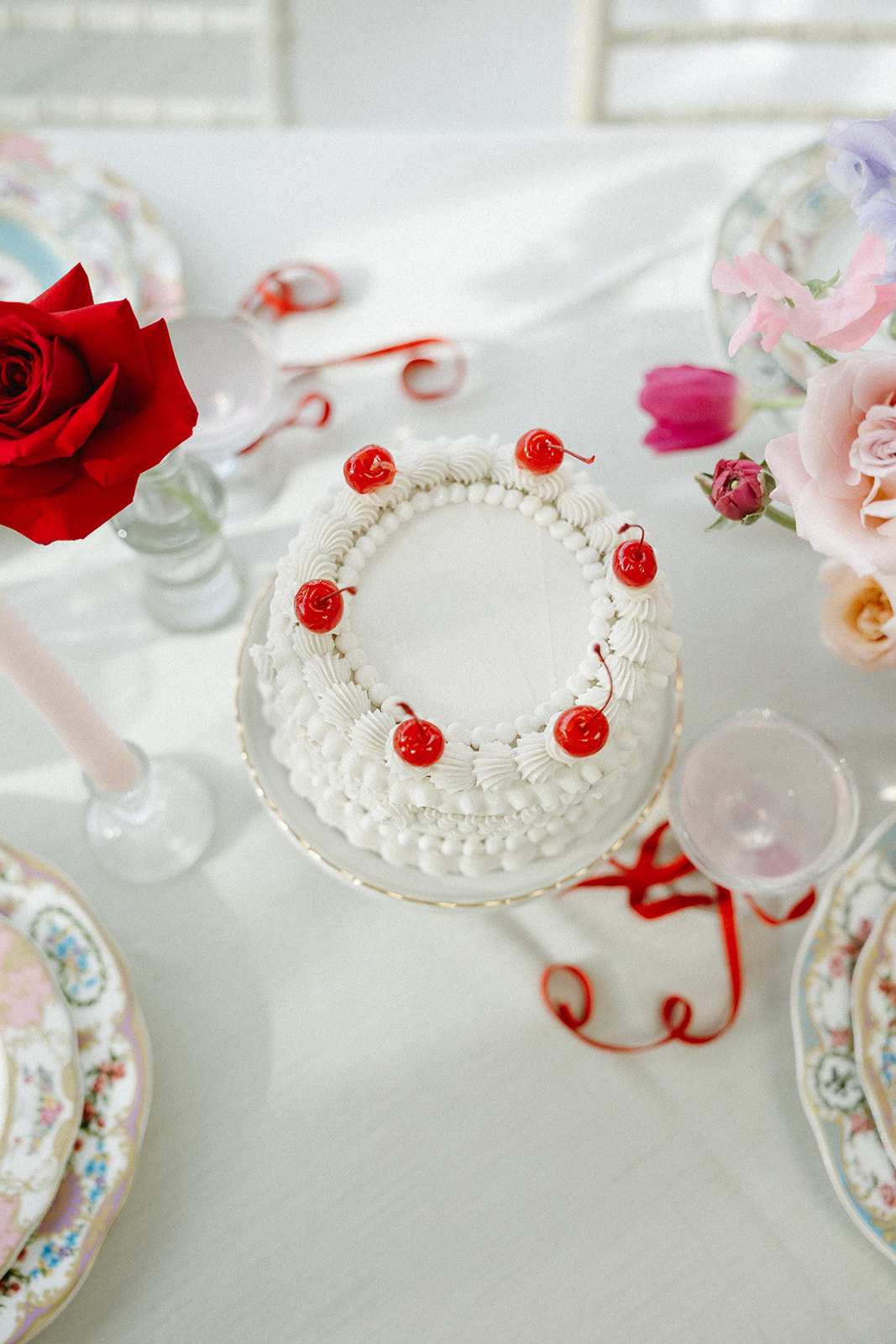 Funky reception setup with vibrant retro-inspired decor and playful design elements like beautiful vintage china, bold coloured candles, and modern flowers. Trendy vintage buttercream wedding cake design with white piped buttercream and cherries on top, perfect for a retro or vintage style wedding.