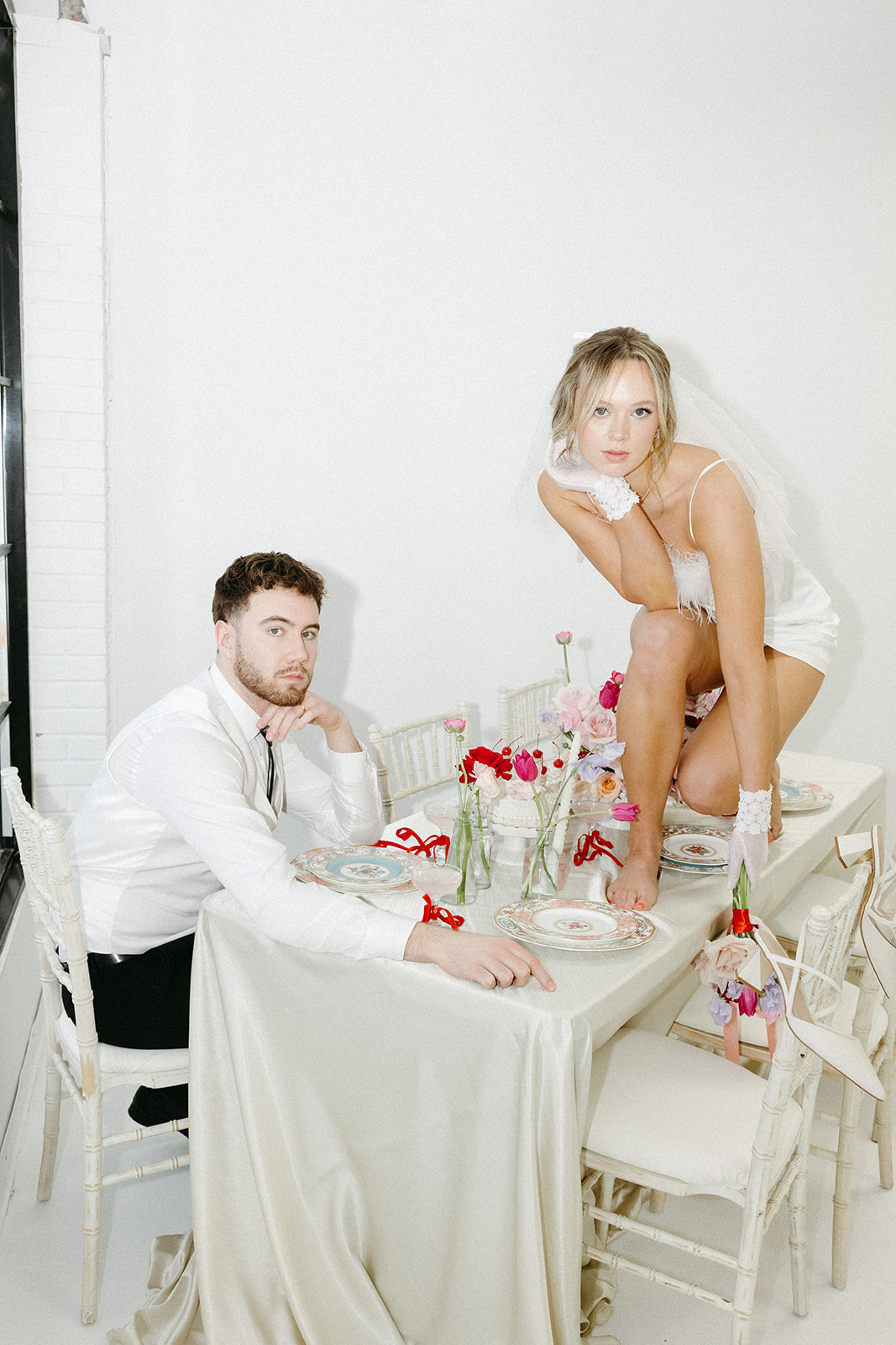 Editorial wedding shoot featuring retro wedding dress and groom’s suit, styled with modern minimalist elements. Funky reception setup with vibrant retro-inspired decor and playful design elements, bold coloured candles, and modern flowers.