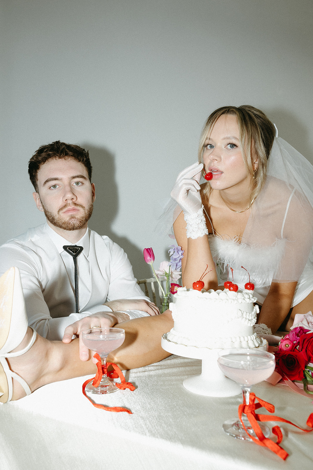 Funky reception setup with vibrant retro-inspired decor and playful design elements like beautiful vintage china, bold coloured candles, and modern flowers. Bride eating cherry from trendy vintage buttercream wedding cake design with white piped buttercream and cherries on top, perfect for a retro or vintage style wedding. 