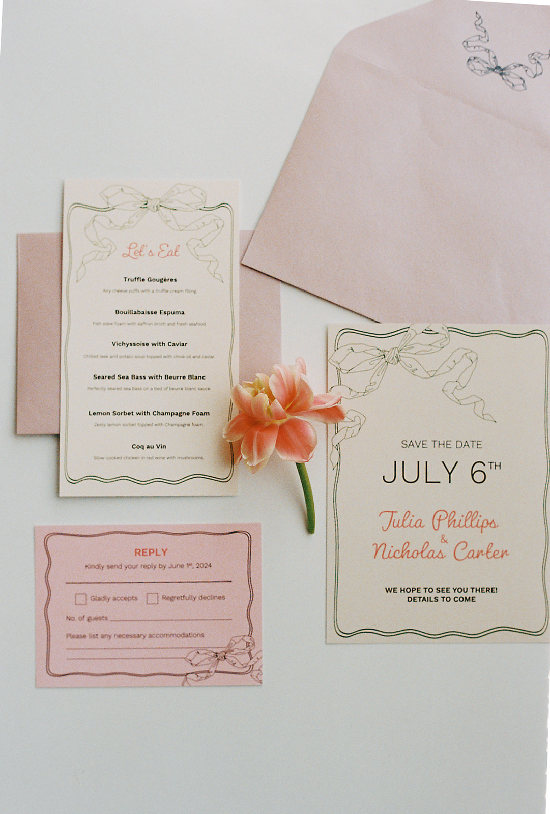 A flat-lay of wedding invitations printed on cream-coloured paper with soft pink and gold accents. The invitations are tied with a delicate ribbon, and an orange lily flower is placed alongside the cards, adding a romantic touch. 