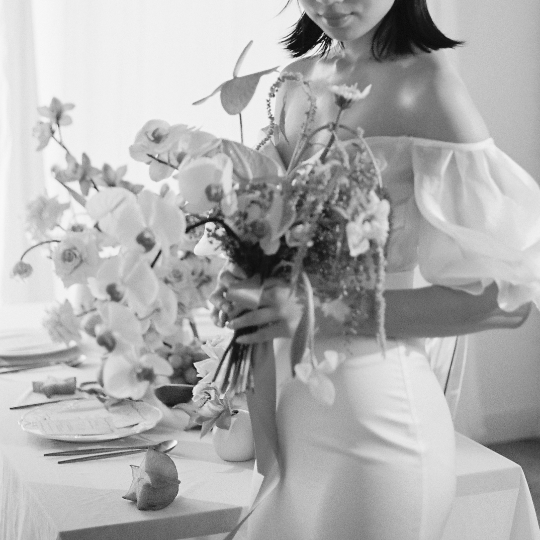 Black and white bridal portrait of elegant spring-inspired bridal look. Bride wearing an off-the-shoulder gown with sheer puffed sleeves holding a large bridal bouquet. 