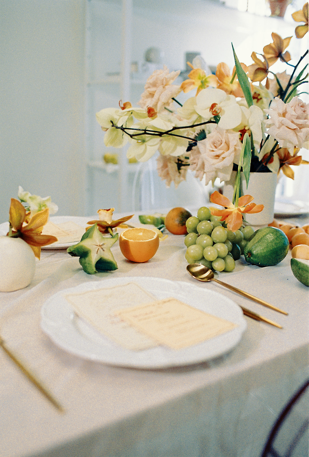 A vibrant close-up of a table arrangement featuring a lush display of flowers in soft peach, orange and cream tones. Citrus Fruit and Florals Wedding Table Centerpiece Inspiration.