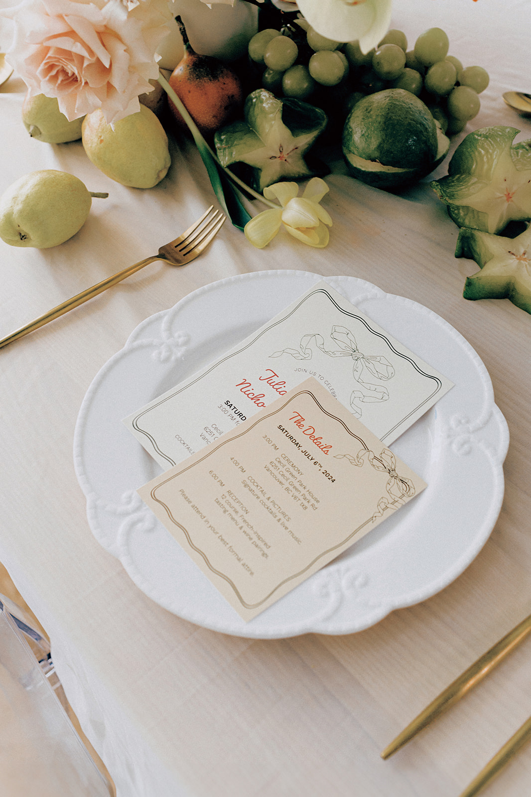 Fruit and Florals Wedding Inspiration with fresh green grapes, apricots and starfruit. Place setting featuring an ornate white dinner plate with a custom wedding menu on top, alongside gold silverware. 