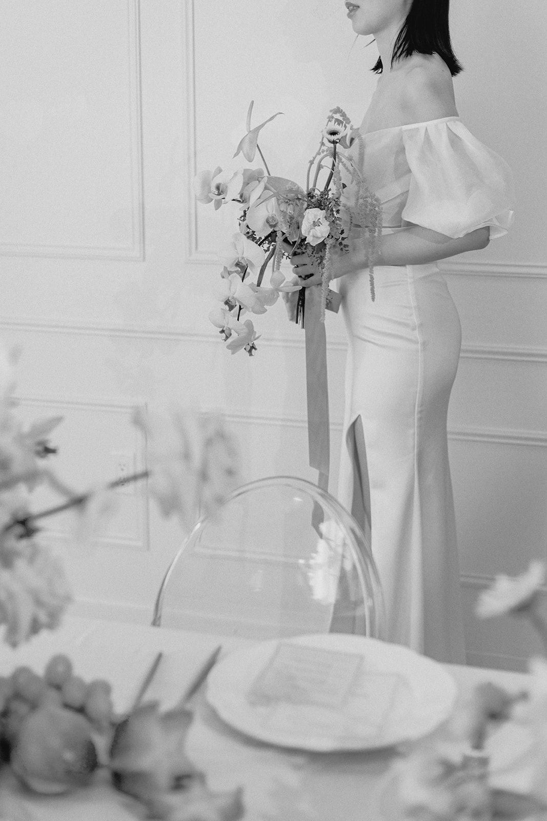 Black and white bridal portrait of elegant spring-inspired bridal look. Bride wearing an off-the-shoulder gown with sheer puffed sleeves holding a large bridal bouquet. 