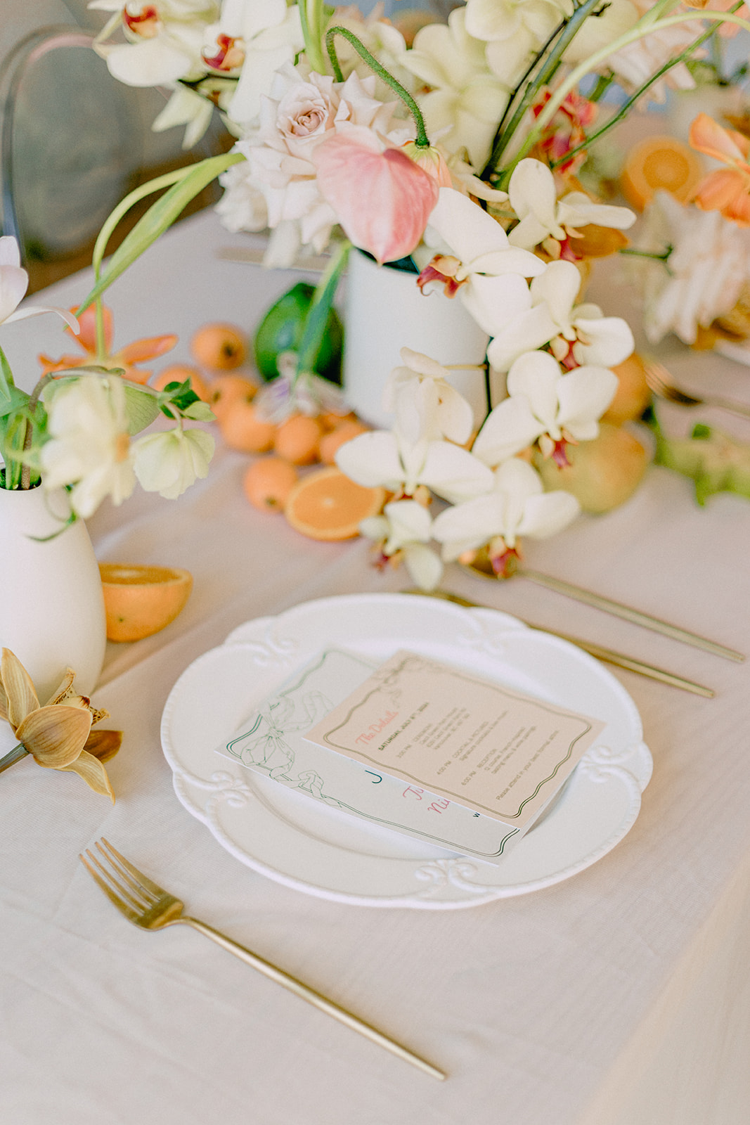 A vibrant close-up of a table arrangement featuring a lush display of flowers in soft peach, orange and cream tones. Fruit and Florals Wedding Inspiration with fresh green grapes, apricots and starfruit.