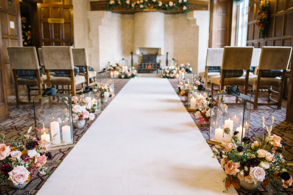 Candles and lush winter florals line the aisle, creating a romantic and intimate setting for the cozy wedding ceremony in the Angus Room at Fairmont Banff Springs,