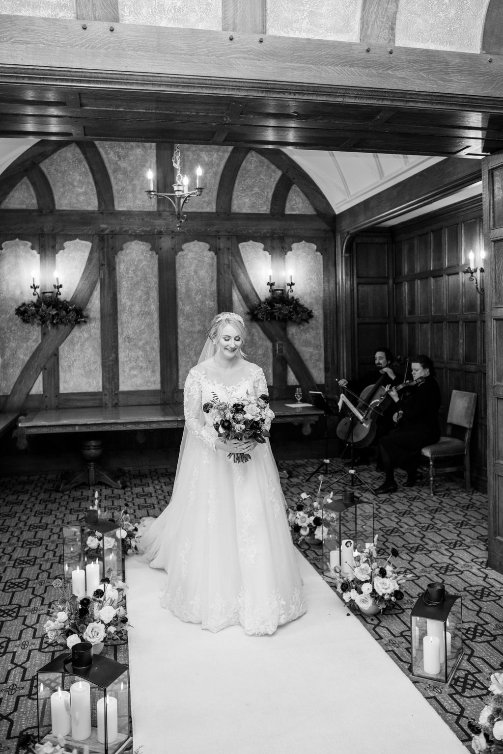 The bride walks down the aisle of the Angus Room, surrounded by rich florals and candlelight in an intimate winter setting.