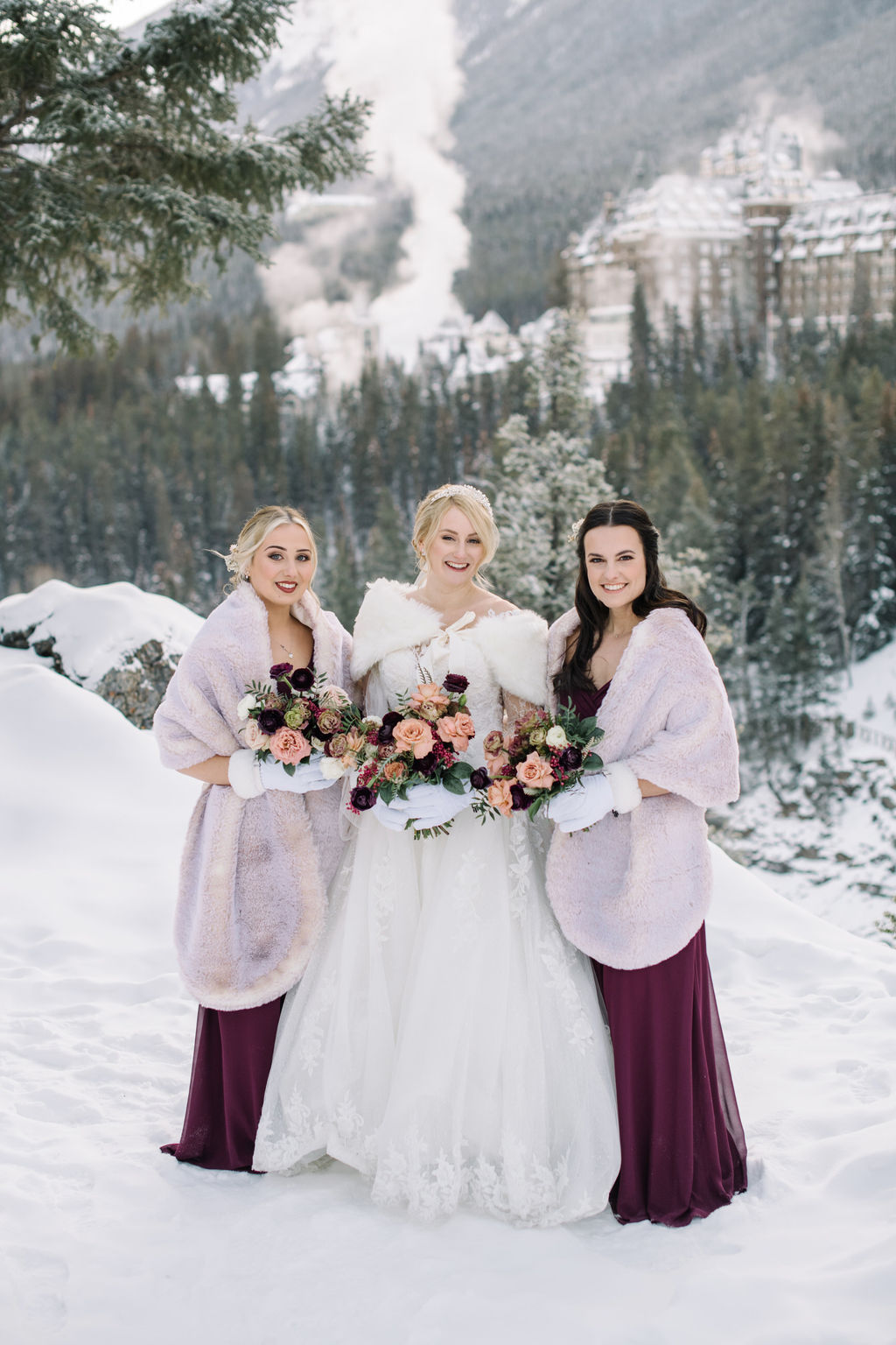Bride and bridal party poses in the snowy mountains with Fairmont Banff Springs behind them.