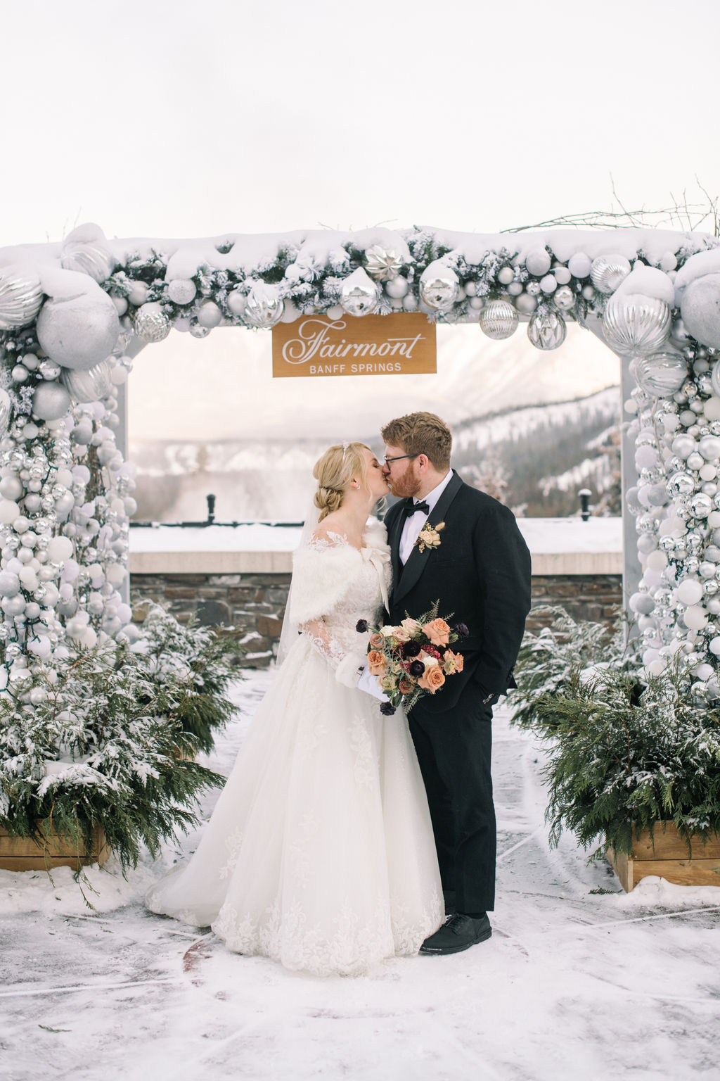 The newlyweds embrace in the snowy courtyard of Fairmont Banff Springs for a beautiful winter wedding portrait.