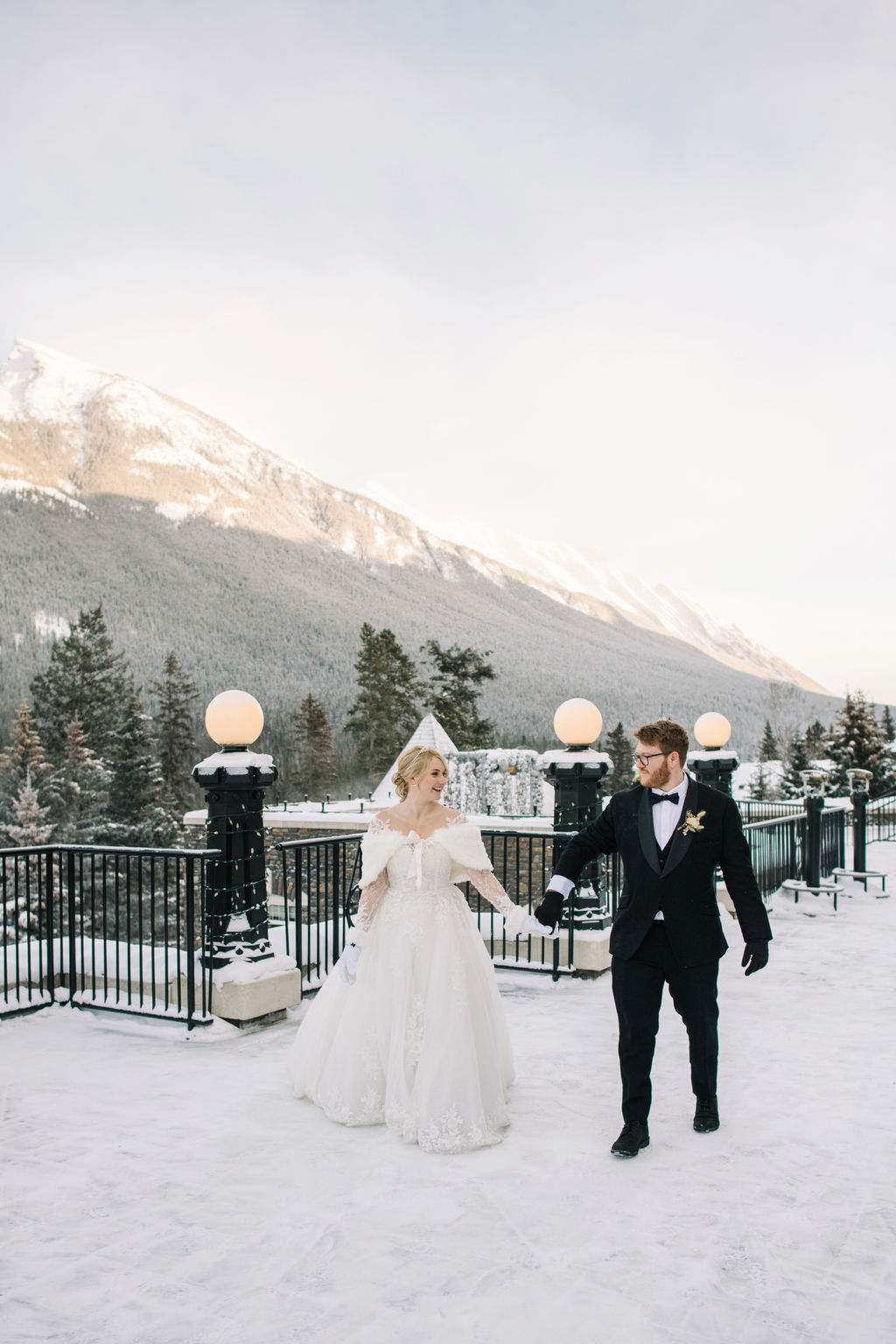 The newlyweds walk on the snowy rooftop patio of Fairmont Banff Springs for a beautiful winter wedding portrait in the Rocky Mountains.