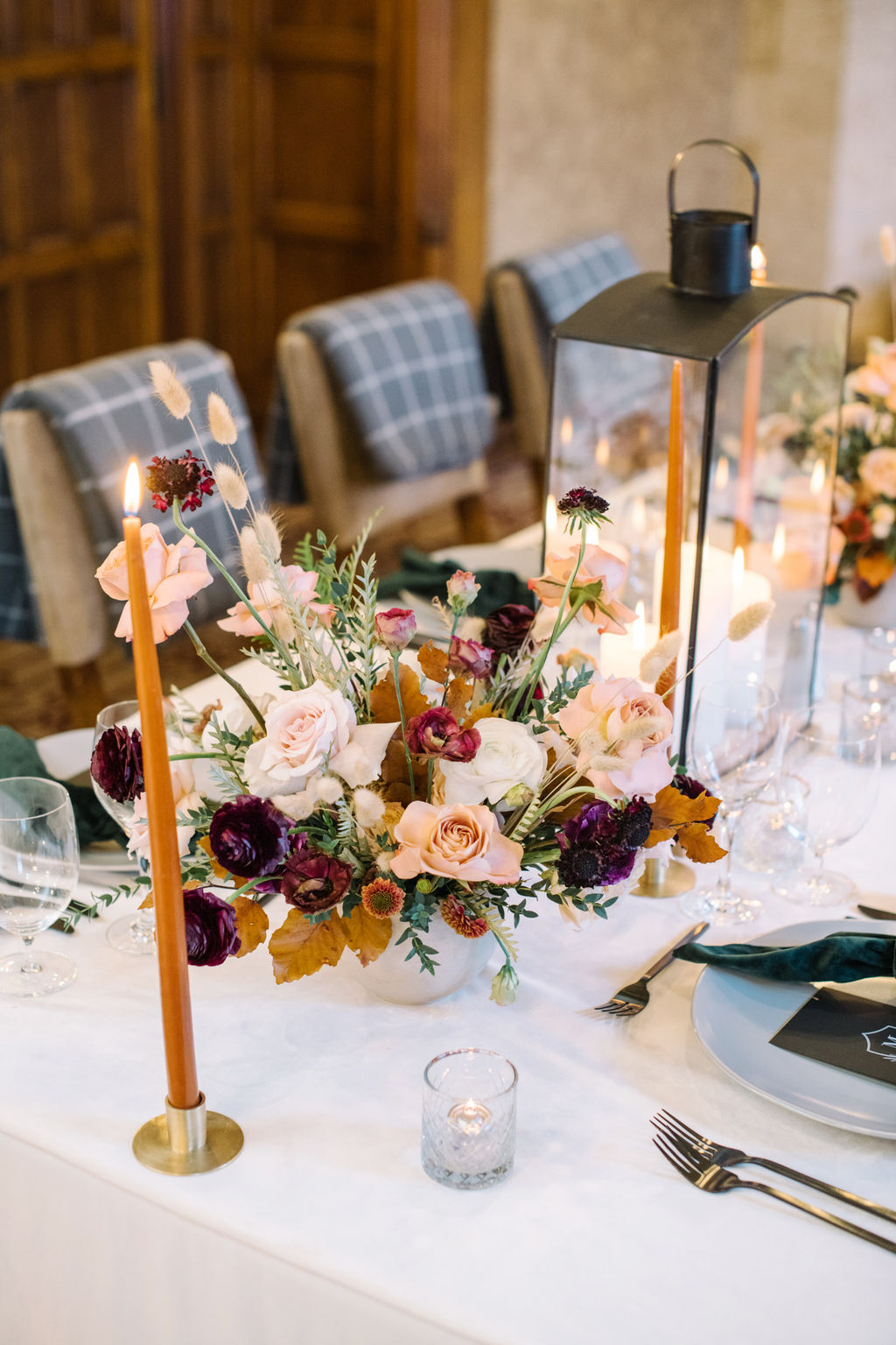 Wedding table set with hunter green velvet napkins, burgundy and blush florals, and glowing candles for a cozy winter wedding aesthetic.
