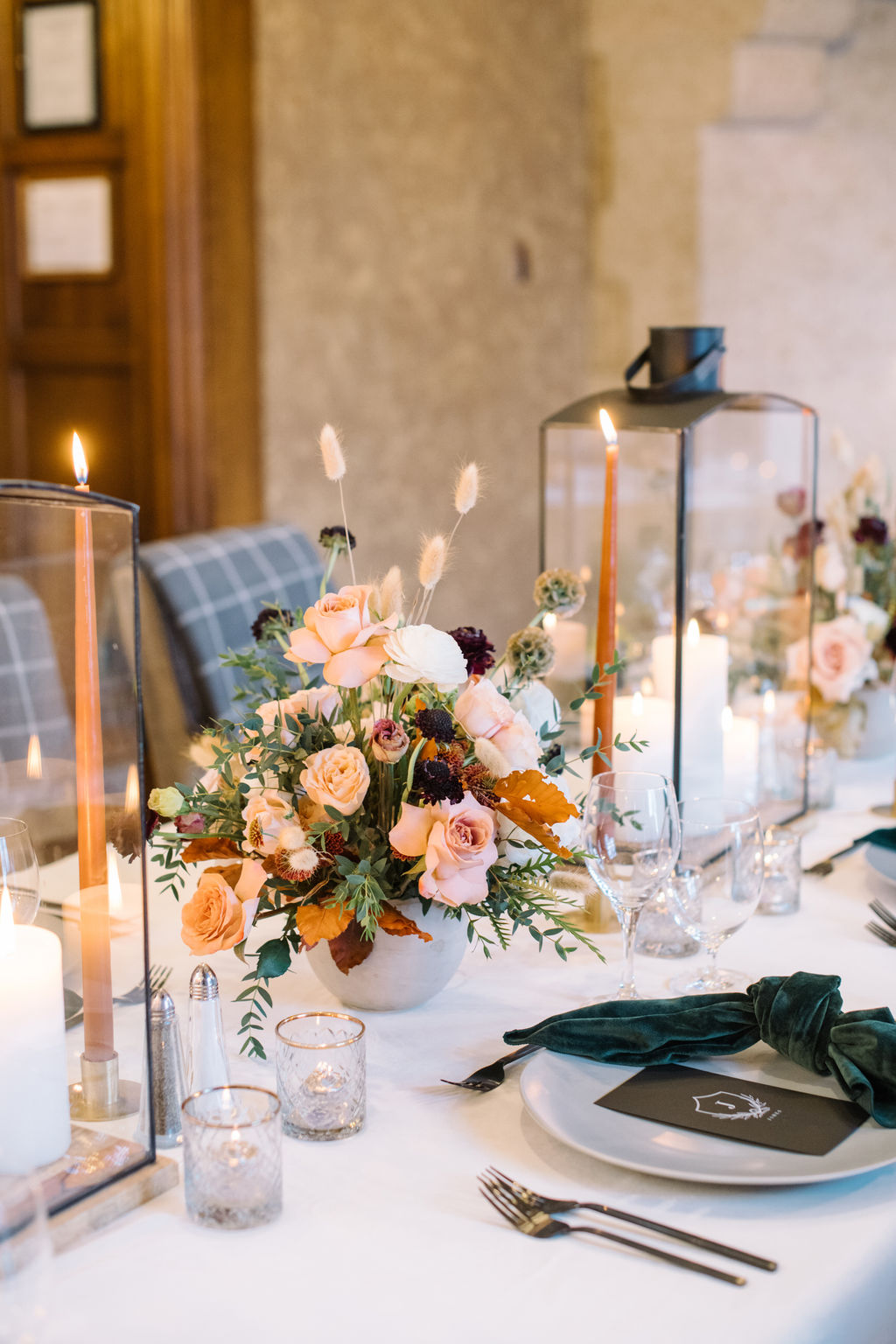 Wedding table set with hunter green velvet napkins, burgundy and blush florals, and glowing candles for a cozy winter wedding aesthetic.
