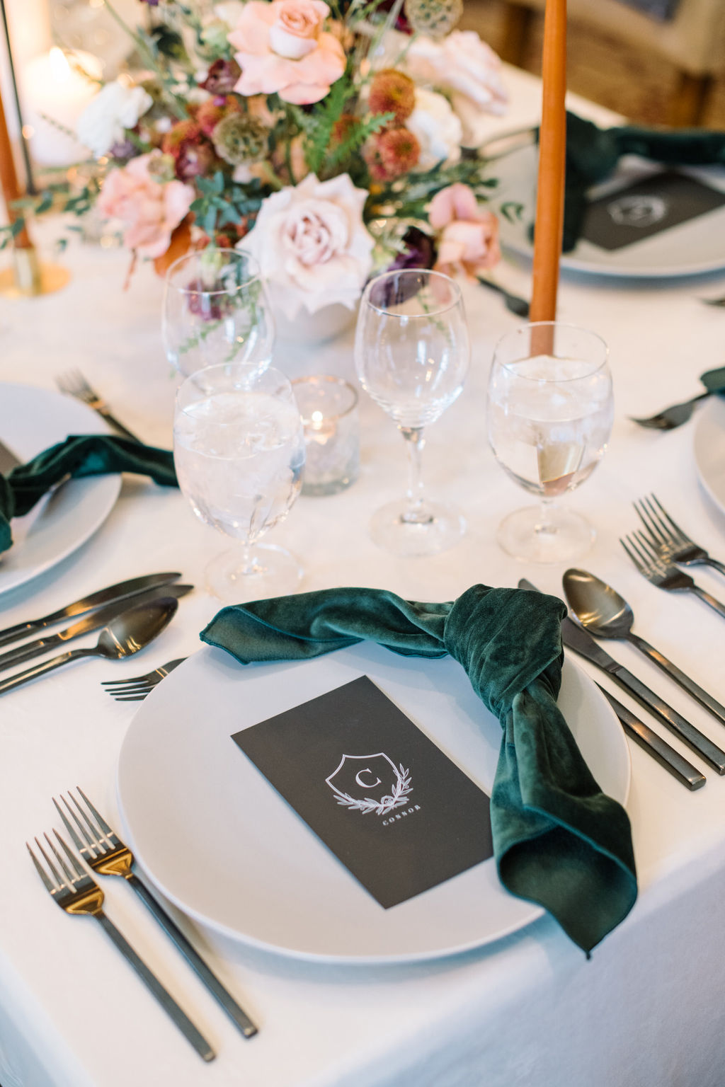 Wedding table set with hunter green velvet napkins, burgundy and blush florals, and glowing candles for a cozy winter wedding aesthetic.