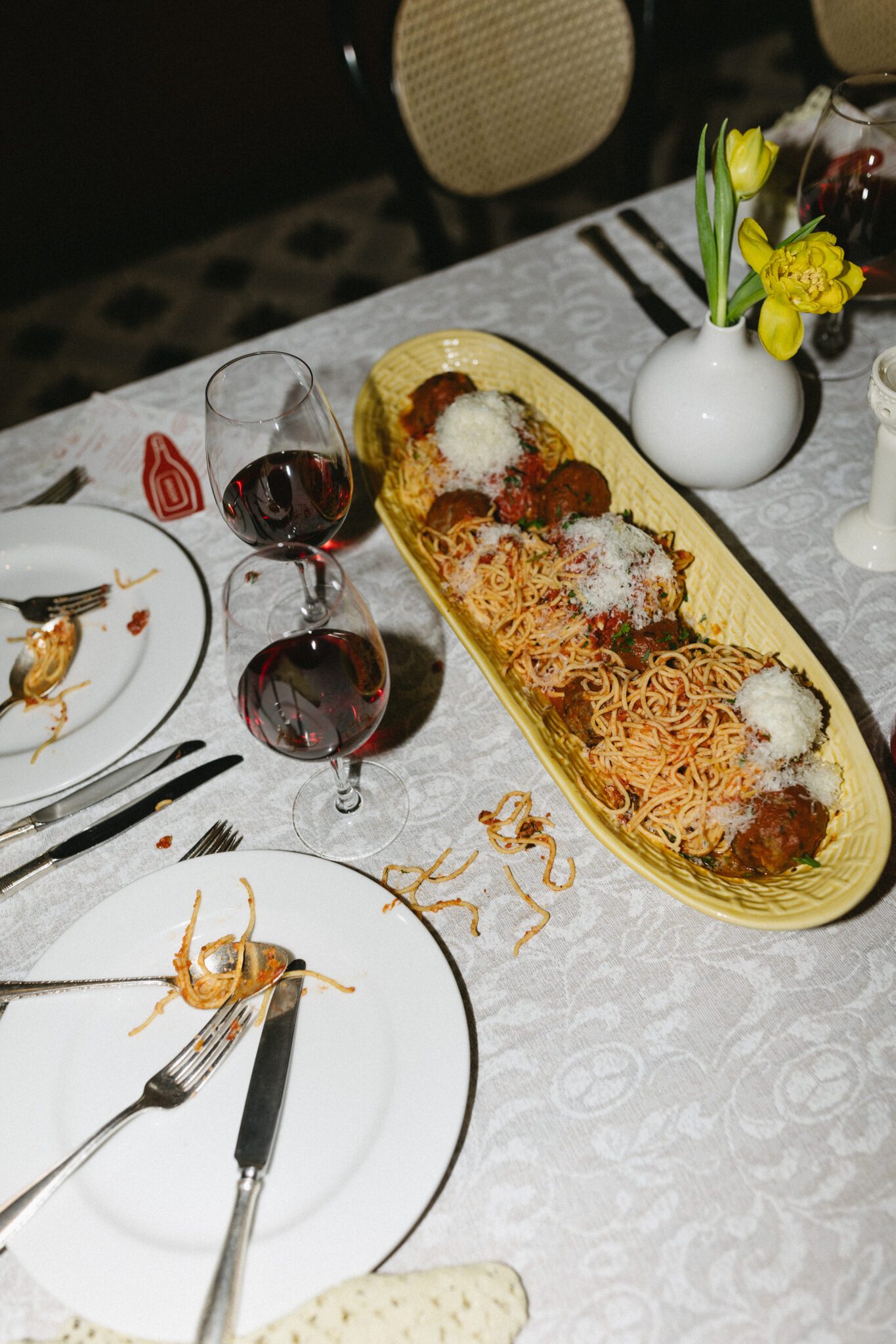 This Italy inspired wedding inspiration at Buffo Restaurant in Calgary, showcases modern sophistication, vintage charm, and a vibrant red colour palette. This photo shows the reception table with food being eat and centerpiece details. #weddingtable #modernweddinginspiration #restaurantreception #vintageweddinginspo