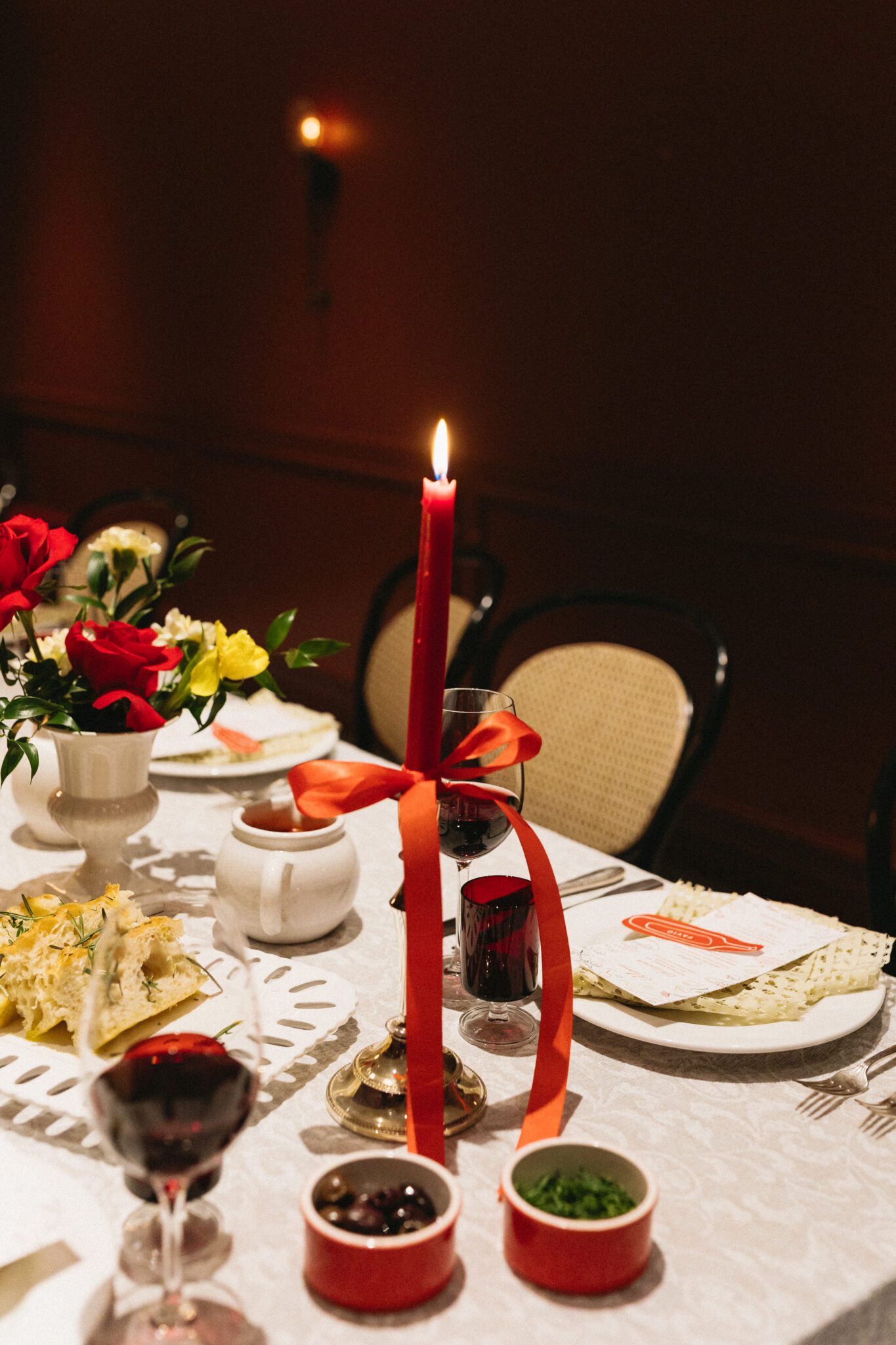 This Italy inspired wedding inspiration at Buffo Restaurant in Calgary, showcases modern sophistication, vintage charm, and a vibrant red colour palette. This photo shows the reception table with food being eat and centerpiece details. #weddingtable #modernweddinginspiration #restaurantreception #vintageweddinginspo