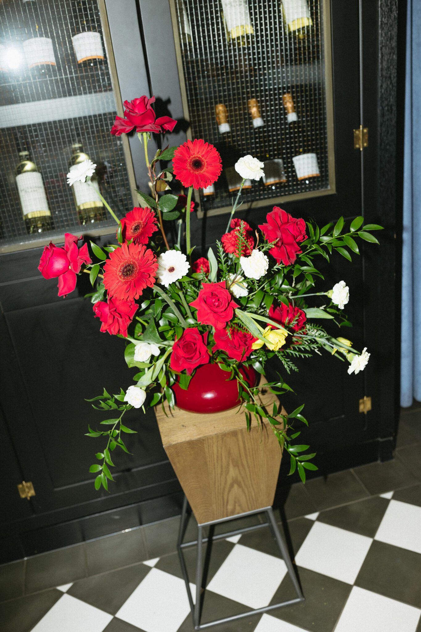 Retro inspired wedding ceremony design with two red rose arrangements with yellow tulips on wooden stands. 