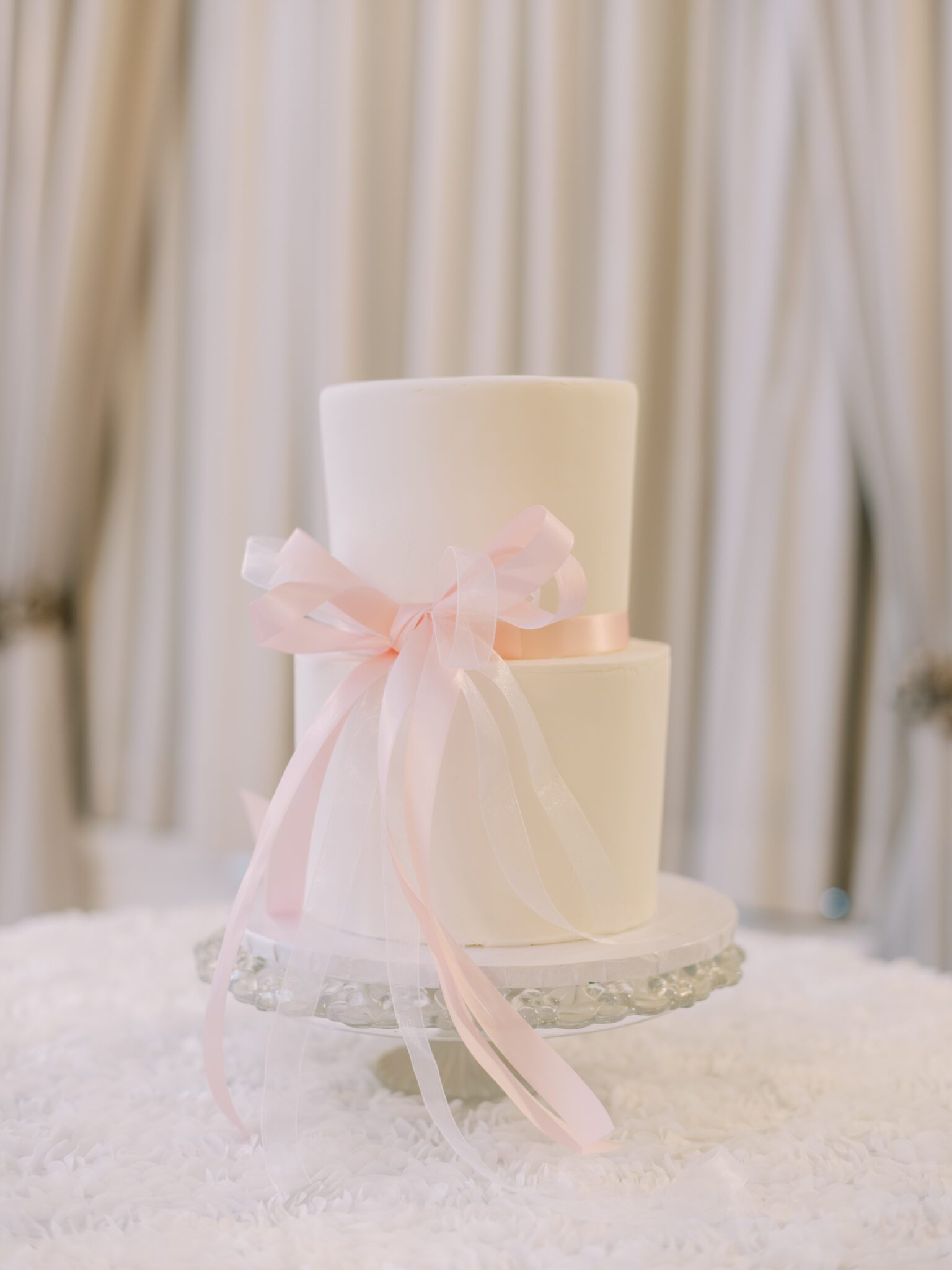 White two-tiered wedding cake with blush pink bow.